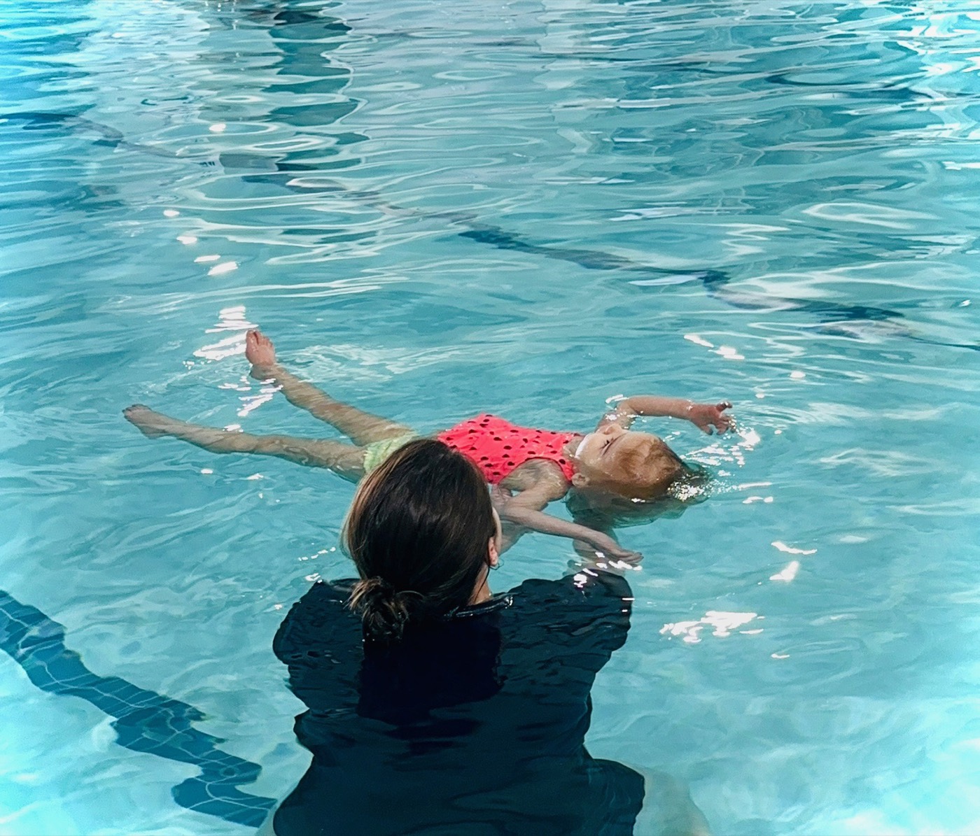 A baby practicing a survival back float, supported by the instructor