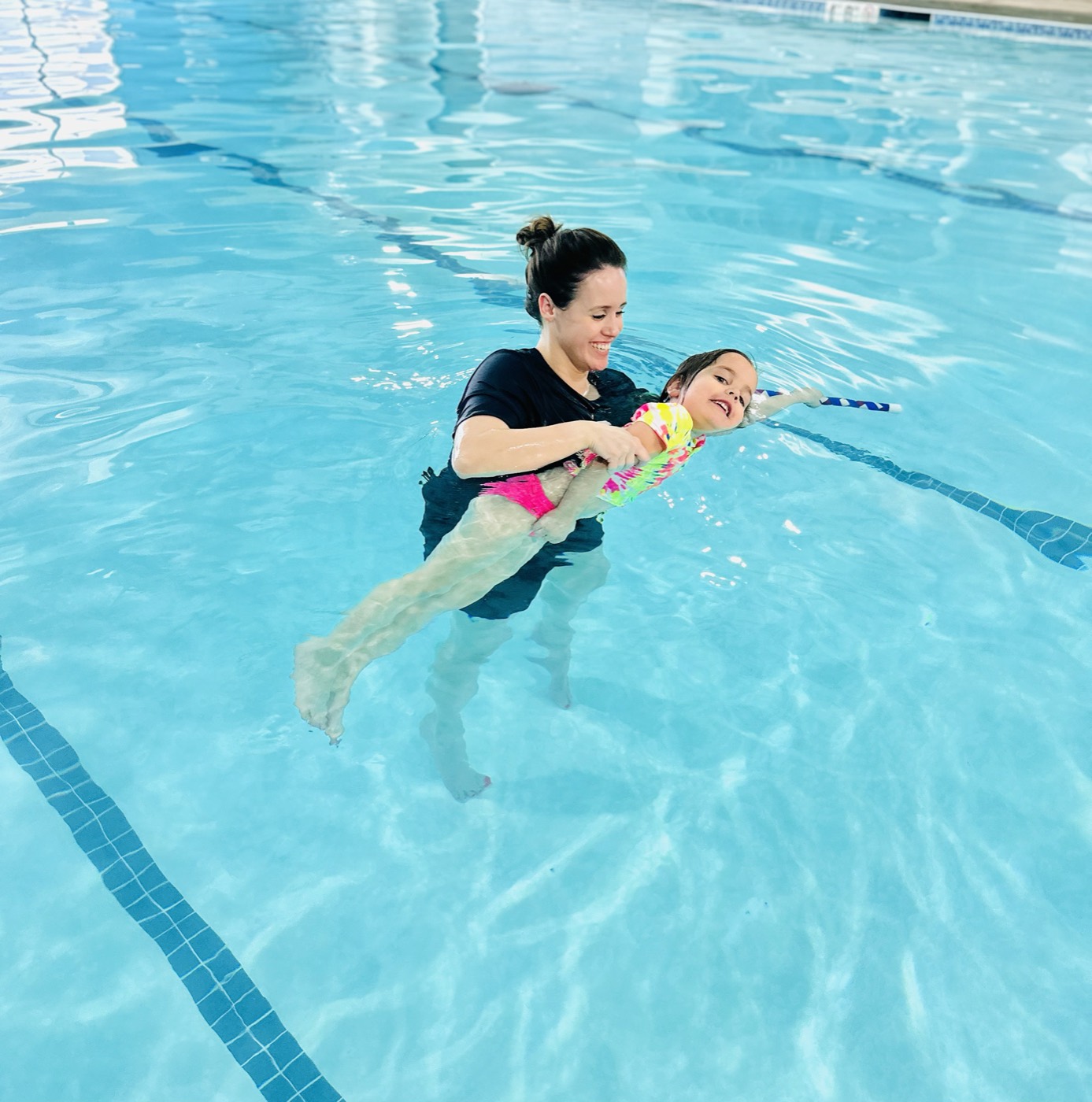 A girl practicing swimming with a kickboard alongside the instructor