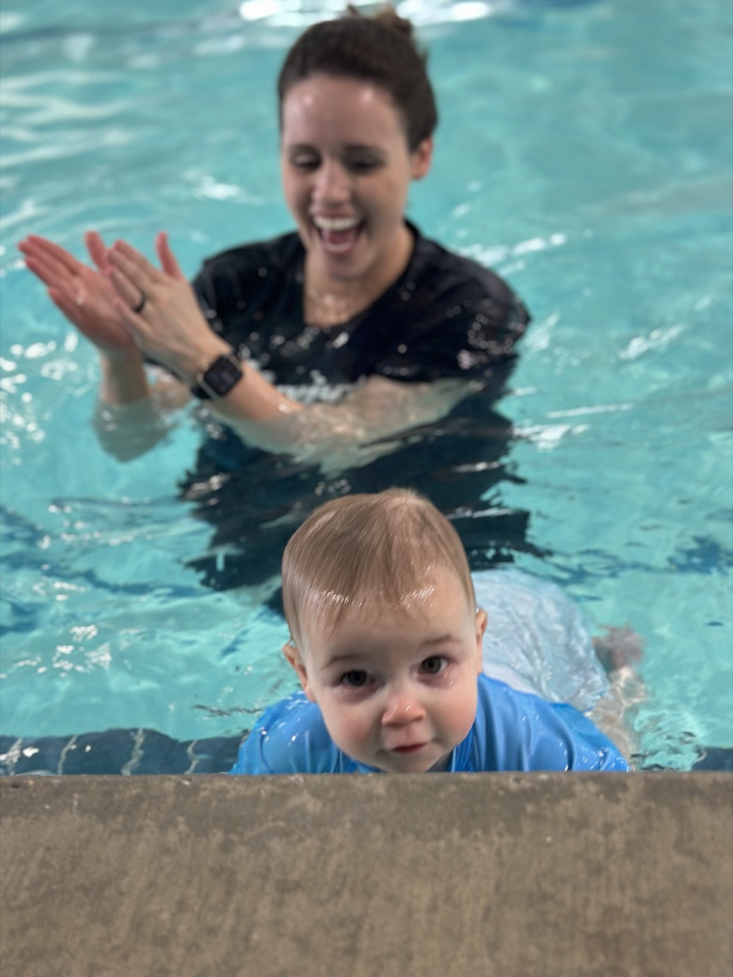 A baby reaching the pool wall while the instructor cheers